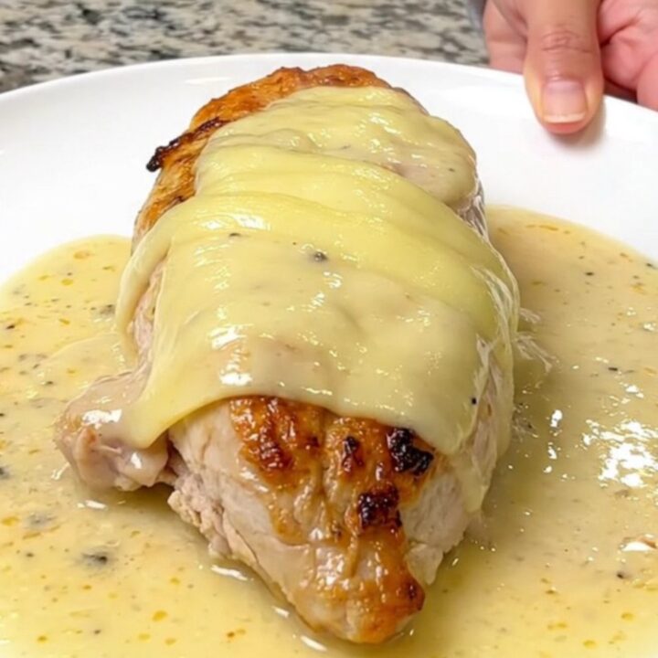 A close-up of tender chicken breasts topped with melted Swiss cheese in a creamy sauce.
