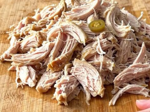 A close-up of shredded chicken piled high on slider buns with pepperoncini peppers.