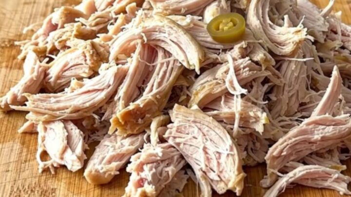 A close-up of shredded chicken piled high on slider buns with pepperoncini peppers.