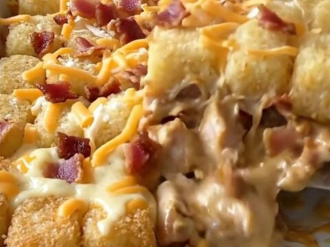 A golden brown chicken bacon ranch potato tot casserole in a white baking dish.