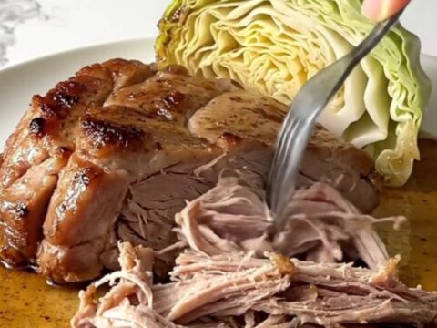 A slow cooker filled with chunks of tender pork shoulder and wedges of cooked green cabbage.