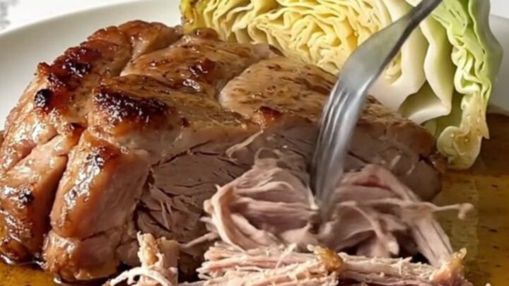 A slow cooker filled with chunks of tender pork shoulder and wedges of cooked green cabbage.