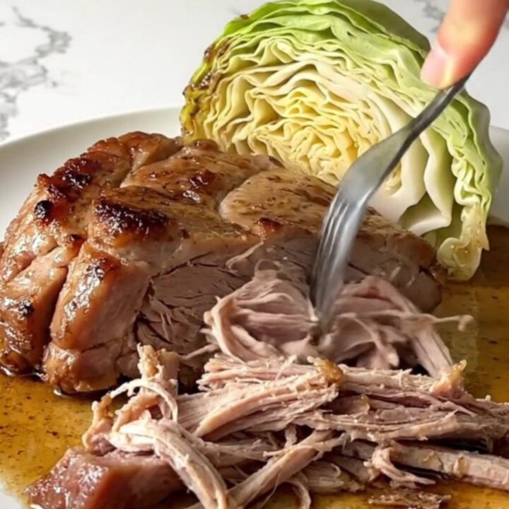 A slow cooker filled with chunks of tender pork shoulder and wedges of cooked green cabbage.