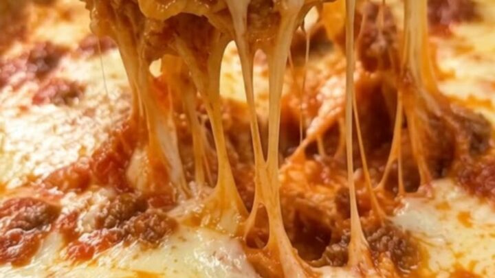 A close-up of a spoon lifting a portion of one-pot skillet lasagna with melted, stretchy mozzarella cheese.