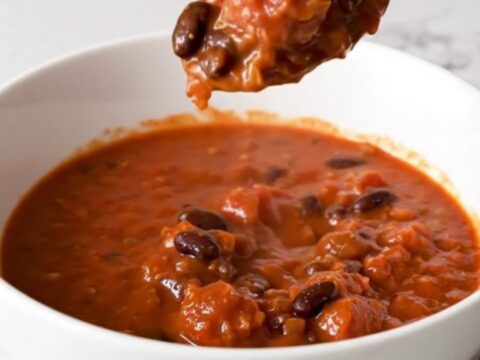 A bowl of rich, red Italian sausage chili with black beans, garnished with fresh herbs.