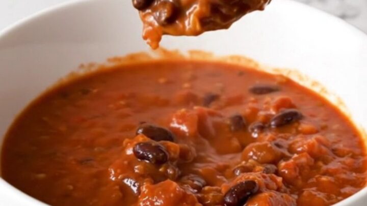 A bowl of rich, red Italian sausage chili with black beans, garnished with fresh herbs.