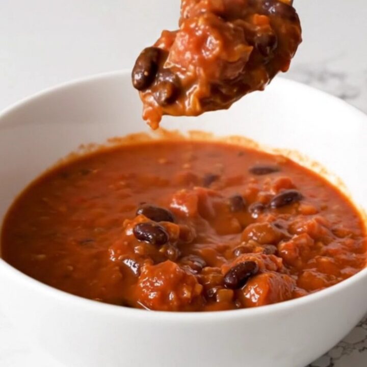 A bowl of rich, red Italian sausage chili with black beans, garnished with fresh herbs.