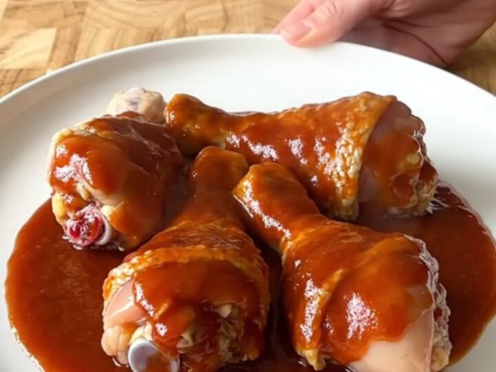 A close-up view of cooked chicken drumsticks in a slow cooker, coated in a thick, glossy red honey gochujang sauce.