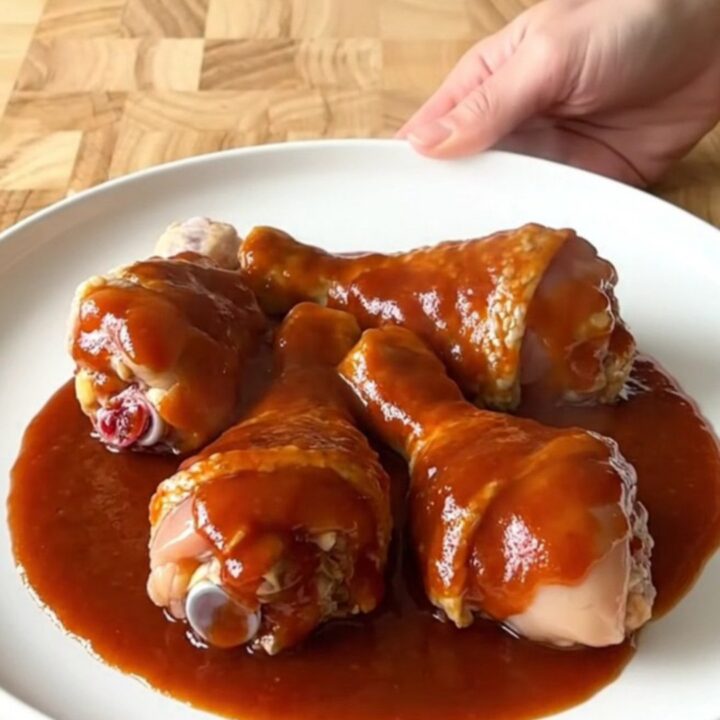 A close-up view of cooked chicken drumsticks in a slow cooker, coated in a thick, glossy red honey gochujang sauce.