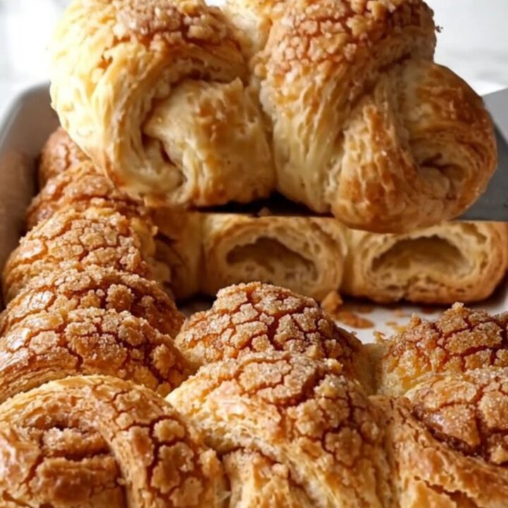 A top-down view of twisted raw crescent roll dough strips arranged in a white ceramic dish on a quartz countertop.