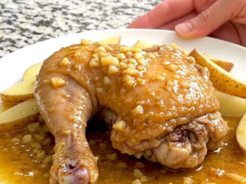 A close-up of tender chicken thighs, soft potato wedges, and green peas in a savory lemon-garlic sauce.