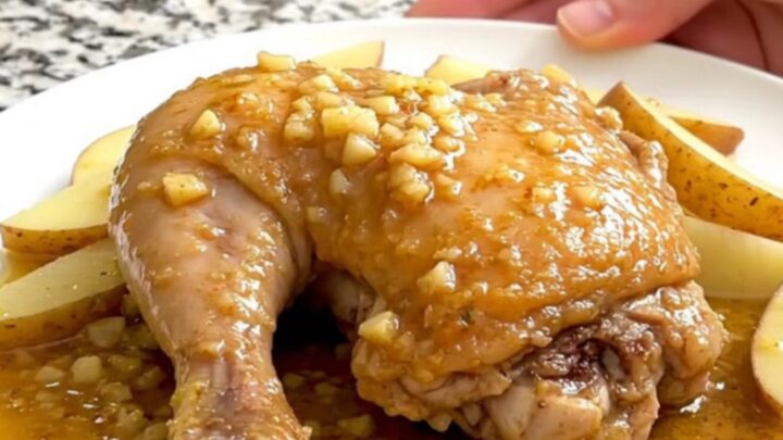 A close-up of tender chicken thighs, soft potato wedges, and green peas in a savory lemon-garlic sauce.