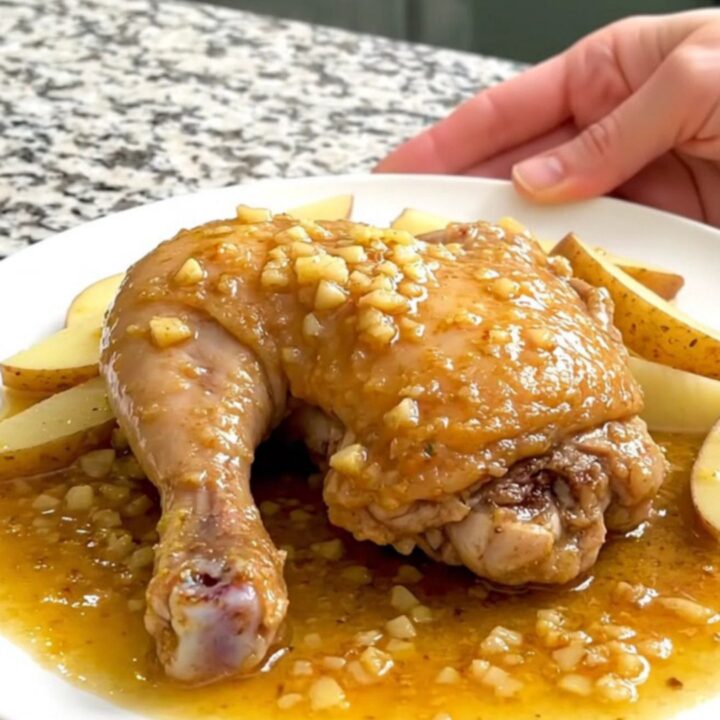 A close-up of tender chicken thighs, soft potato wedges, and green peas in a savory lemon-garlic sauce.
