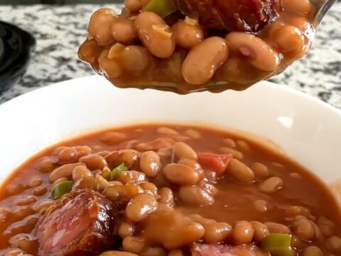 A slow cooker filled with a hearty mix of sliced smoked sausage, pinto beans, diced tomatoes, and onions in a savory sauce.