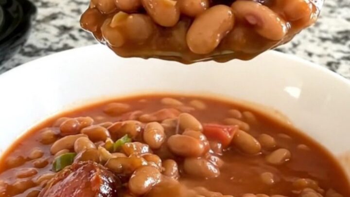 A slow cooker filled with a hearty mix of sliced smoked sausage, pinto beans, diced tomatoes, and onions in a savory sauce.