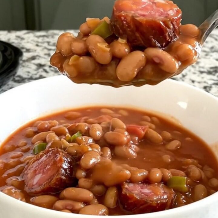 A slow cooker filled with a hearty mix of sliced smoked sausage, pinto beans, diced tomatoes, and onions in a savory sauce.