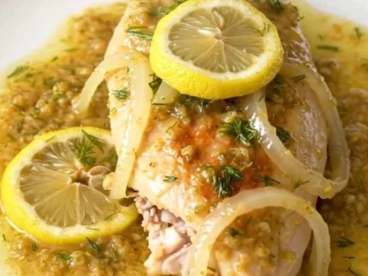 A close-up of tender, slow-cooked lemon dill chicken breasts served on a plain white plate.