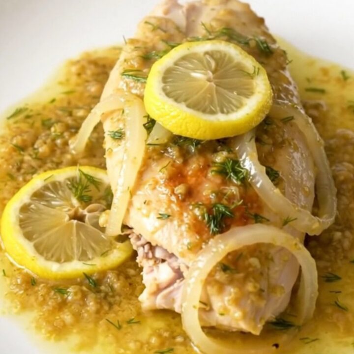 A close-up of tender, slow-cooked lemon dill chicken breasts served on a plain white plate.