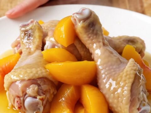 A plate of tender, glazed chicken drumsticks with soft peach slices and a sticky hot honey sauce.
