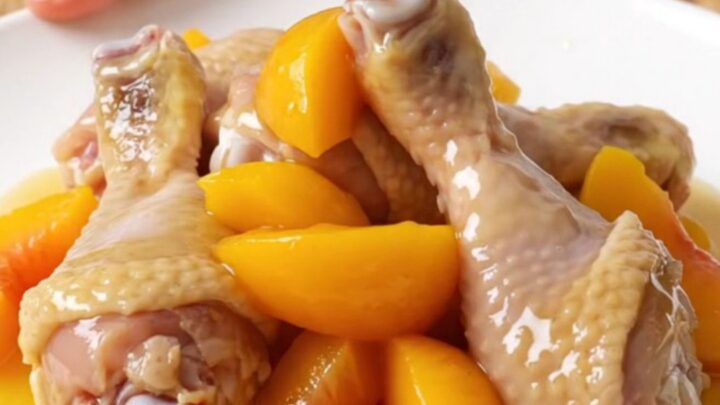 A plate of tender, glazed chicken drumsticks with soft peach slices and a sticky hot honey sauce.