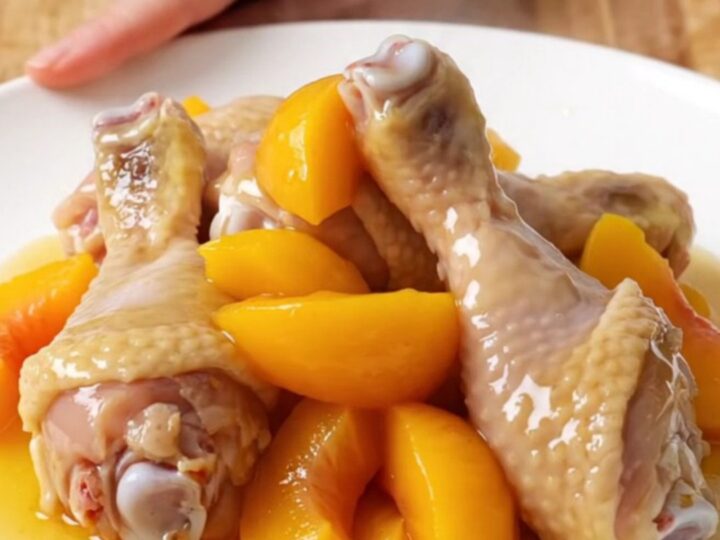 A plate of tender, glazed chicken drumsticks with soft peach slices and a sticky hot honey sauce.