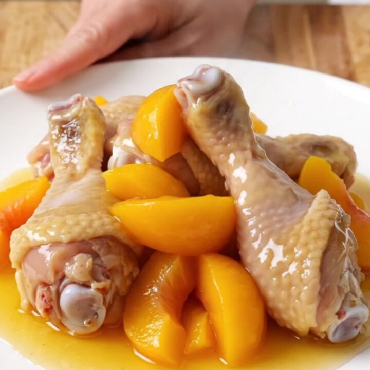 A plate of tender, glazed chicken drumsticks with soft peach slices and a sticky hot honey sauce.