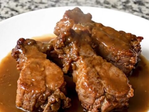A serving of tender pork tips in a rich brown gravy on a white plate.