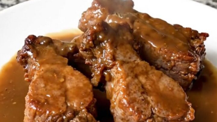 A serving of tender pork tips in a rich brown gravy on a white plate.