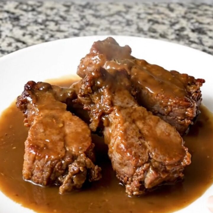 A serving of tender pork tips in a rich brown gravy on a white plate.