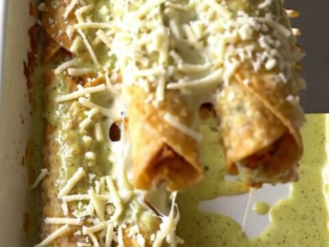 A top-down view of a rectangular baking dish filled with rows of golden-brown chicken taquitos covered in creamy green sauce