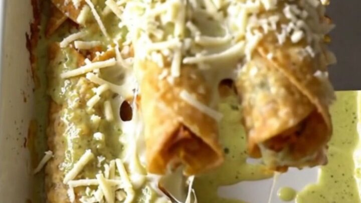 A top-down view of a rectangular baking dish filled with rows of golden-brown chicken taquitos covered in creamy green sauce
