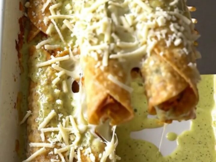 A top-down view of a rectangular baking dish filled with rows of golden-brown chicken taquitos covered in creamy green sauce