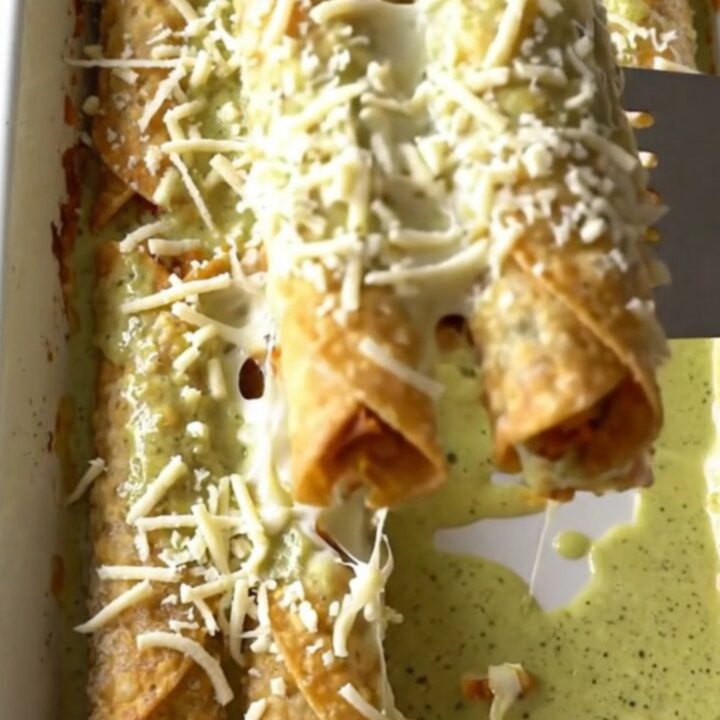 A top-down view of a rectangular baking dish filled with rows of golden-brown chicken taquitos covered in creamy green sauce