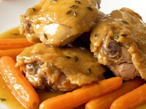 A close-up of tender chicken thighs and bright orange baby carrots in a honey thyme glaze.