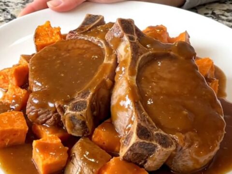 Close up of tender pork chops and sweet potato cubes glazed in a rich brown sugar sauce in a slow cooker.