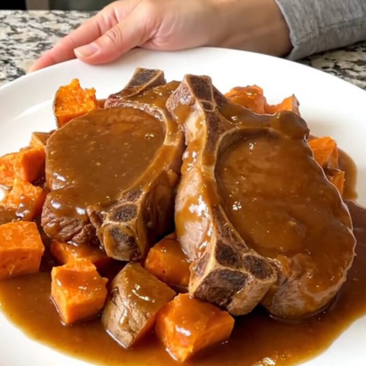 Close up of tender pork chops and sweet potato cubes glazed in a rich brown sugar sauce in a slow cooker.