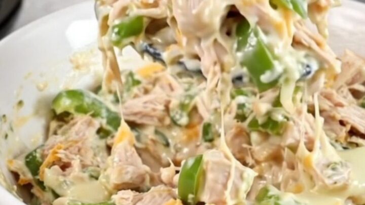 A close-up of creamy chicken cheesesteak dip in a black slow cooker with melted cheese and peppers.