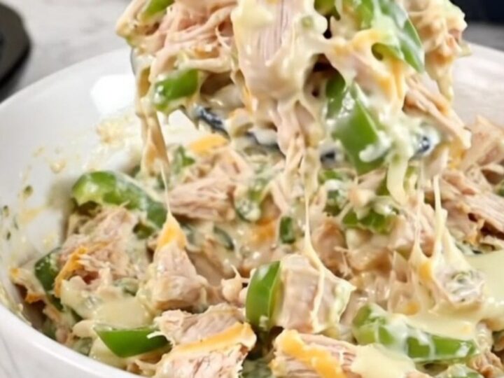 A close-up of creamy chicken cheesesteak dip in a black slow cooker with melted cheese and peppers.