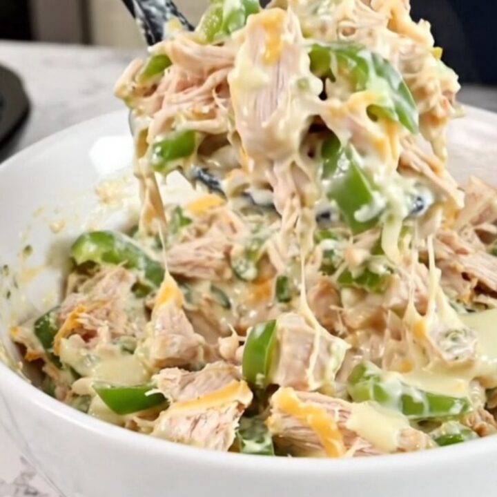 A close-up of creamy chicken cheesesteak dip in a black slow cooker with melted cheese and peppers.