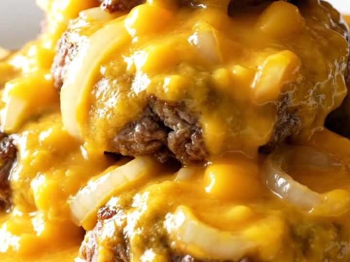 A close-up of tender beef patties smothered in a rich, creamy cheddar cheese sauce in a slow cooker.