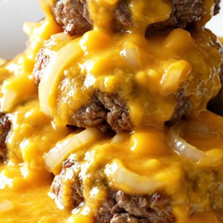 A close-up of tender beef patties smothered in a rich, creamy cheddar cheese sauce in a slow cooker.