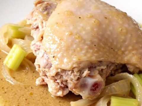 A close-up of tender, slow-cooked turkey thighs covered in a rich, creamy gravy with soft onion and celery pieces.