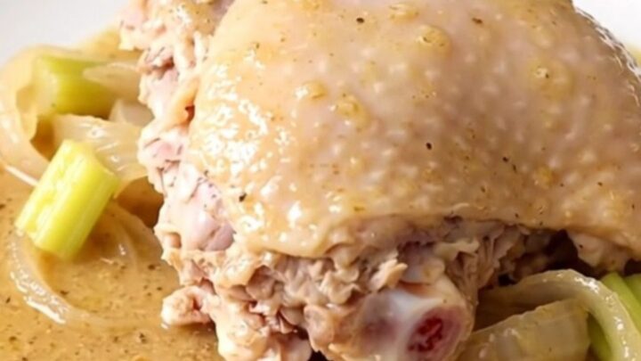 A close-up of tender, slow-cooked turkey thighs covered in a rich, creamy gravy with soft onion and celery pieces.