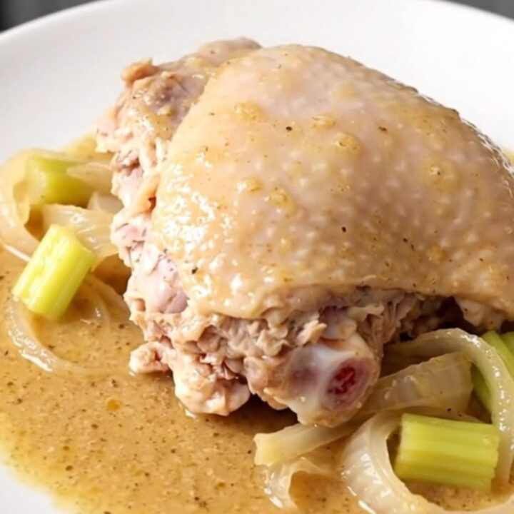 A close-up of tender, slow-cooked turkey thighs covered in a rich, creamy gravy with soft onion and celery pieces.