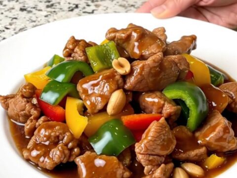 A top-down view of a slow cooker filled with tender kung pao pork, colorful bell peppers, and roasted peanuts.