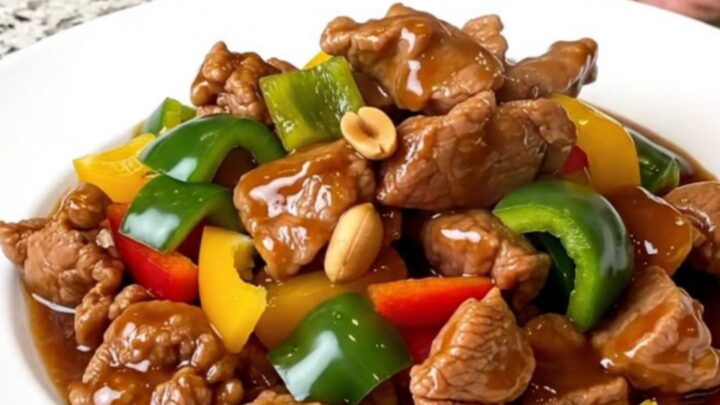 A top-down view of a slow cooker filled with tender kung pao pork, colorful bell peppers, and roasted peanuts.