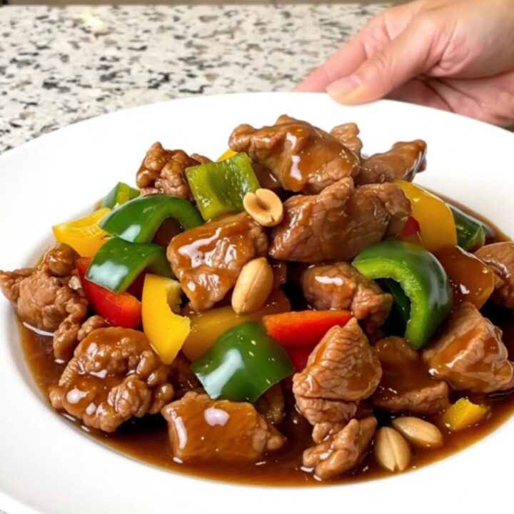 A top-down view of a slow cooker filled with tender kung pao pork, colorful bell peppers, and roasted peanuts.