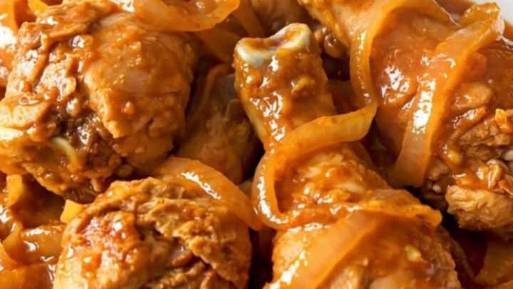 Close-up of slow-cooked Tandoori chicken drumsticks with spiced red sauce and onions.
