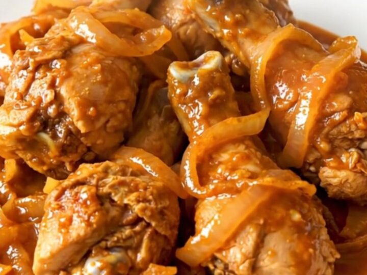 Close-up of slow-cooked Tandoori chicken drumsticks with spiced red sauce and onions.