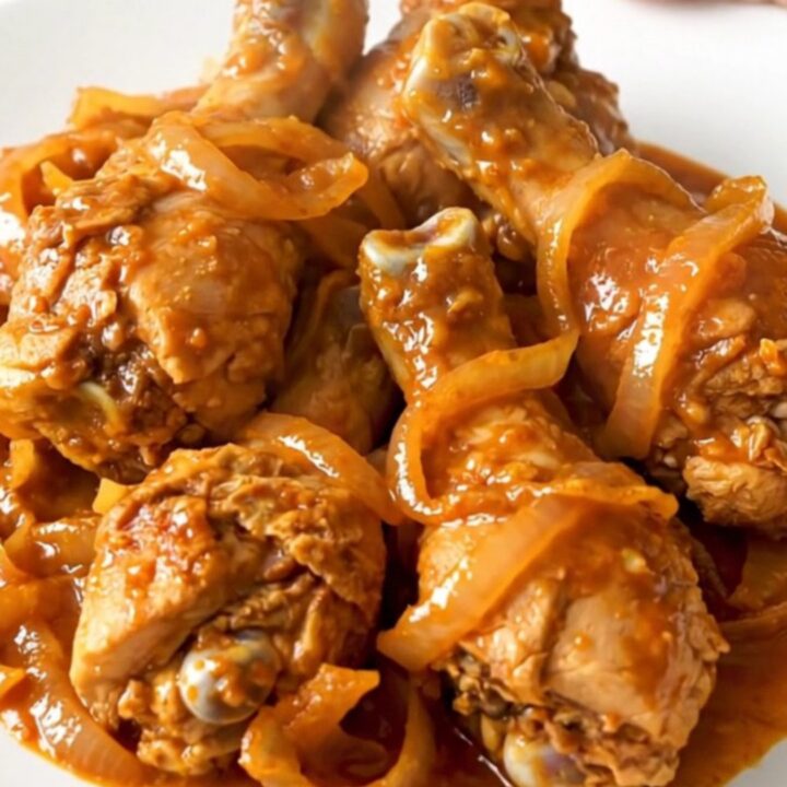 Close-up of slow-cooked Tandoori chicken drumsticks with spiced red sauce and onions.